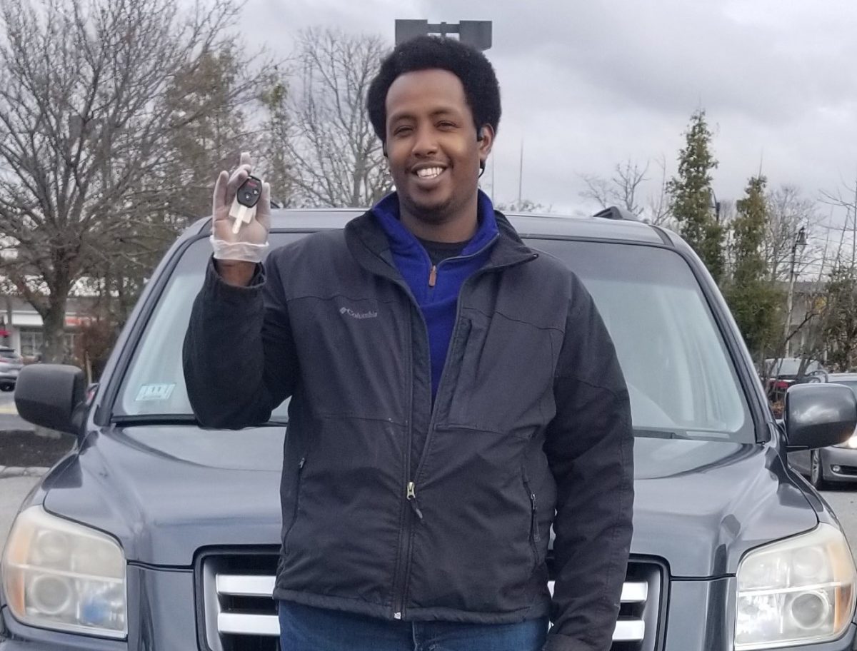Donated car recipient Ahmed smiles for the camera holding the keys to his new SUV.
